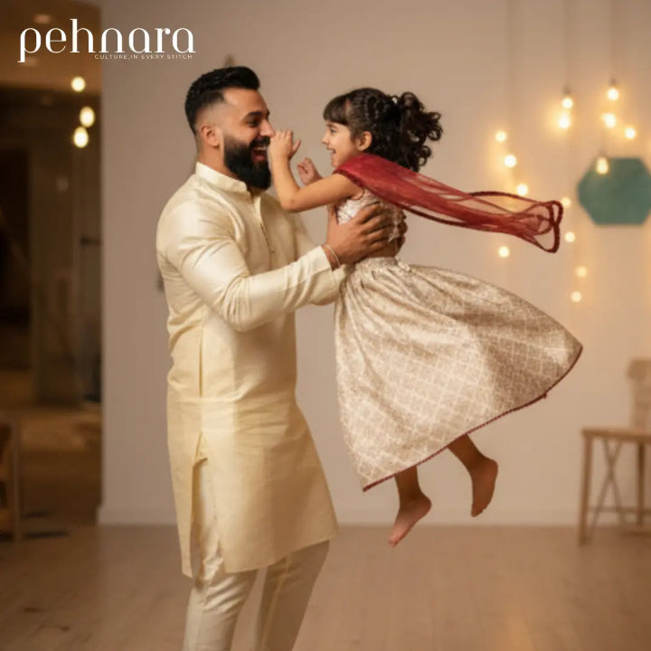 Man in traditional outfit holding a child in a sparkly dress with decorative lights in the background