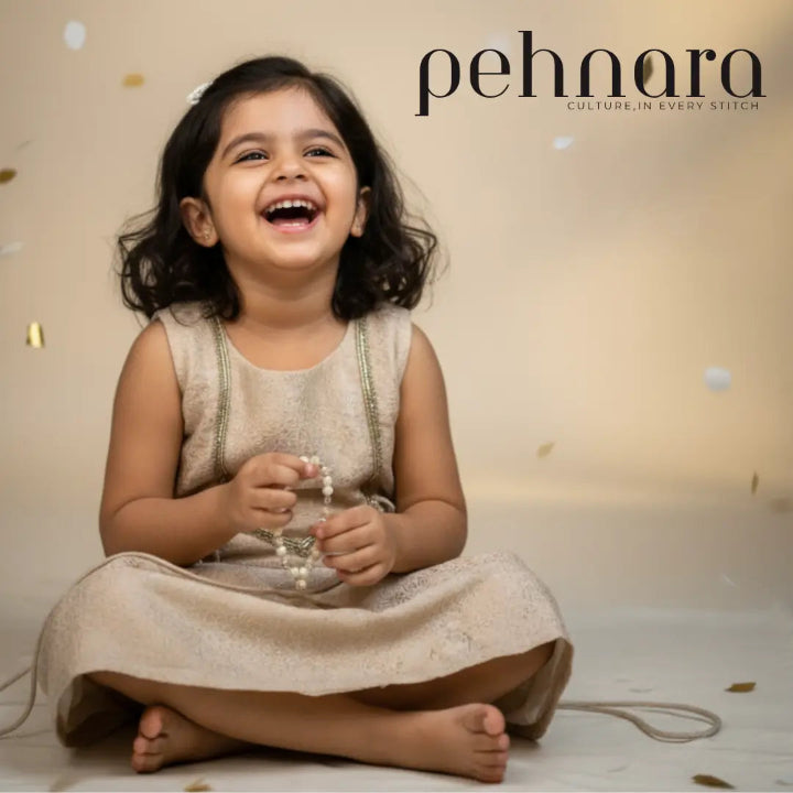 Child in a beige dress sitting on the floor with 'pehnara' branding in the background