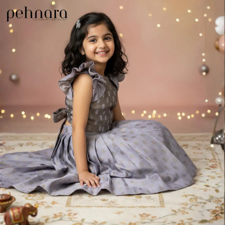 Young girl in a gray dress sitting on a patterned rug with decorative lights in the background, featuring the brand 'pehnara'.