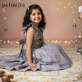 Young girl in a gray dress sitting on a patterned rug with decorative lights in the background, featuring the brand 'pehnara'.