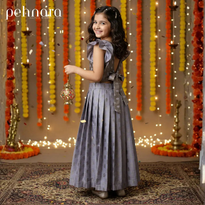 Young girl in a gray dress holding a lantern in a decorated room with lights and flowers.