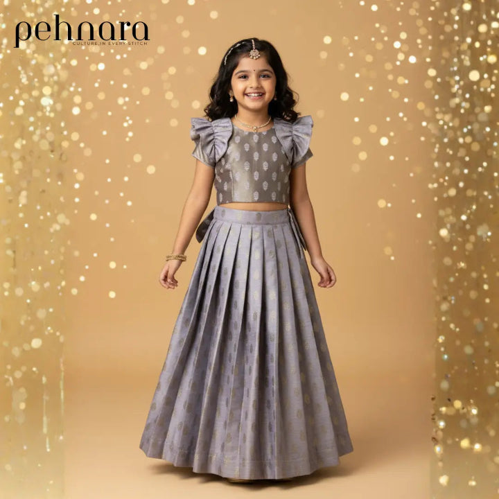 Young girl in a gray traditional outfit with ruffled sleeves against a gold glittery background, featuring the brand 'pehnara'.