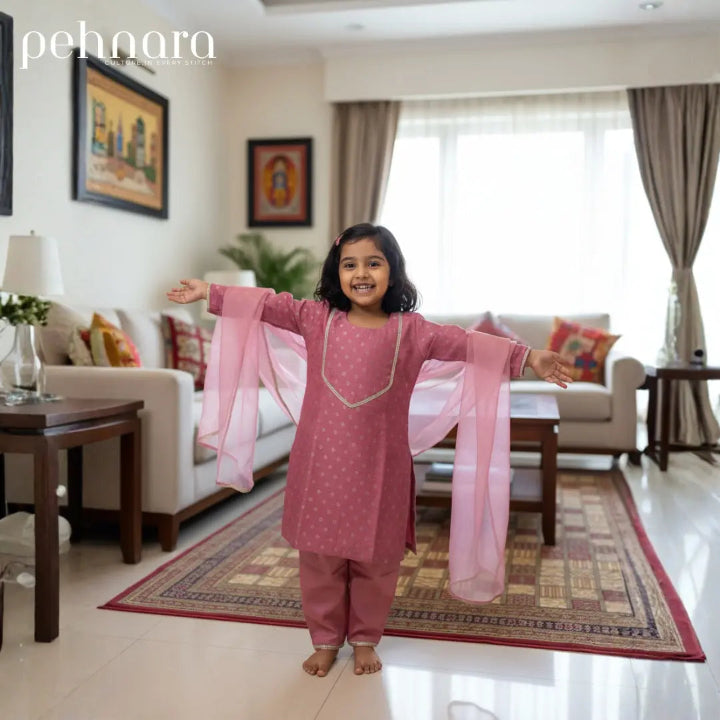 Child in a pink traditional outfit standing in a living room with 'pehnara' branding.