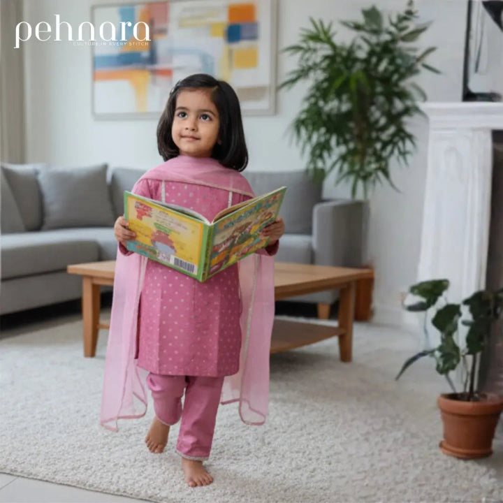 Child in pink traditional outfit reading a book in a living room.