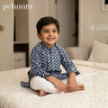 Child wearing a blue patterned shirt sitting on a bed in a bedroom.