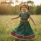 Young girl in a green dress with red trim running through a field of flowers, with 'pehnara' branding.